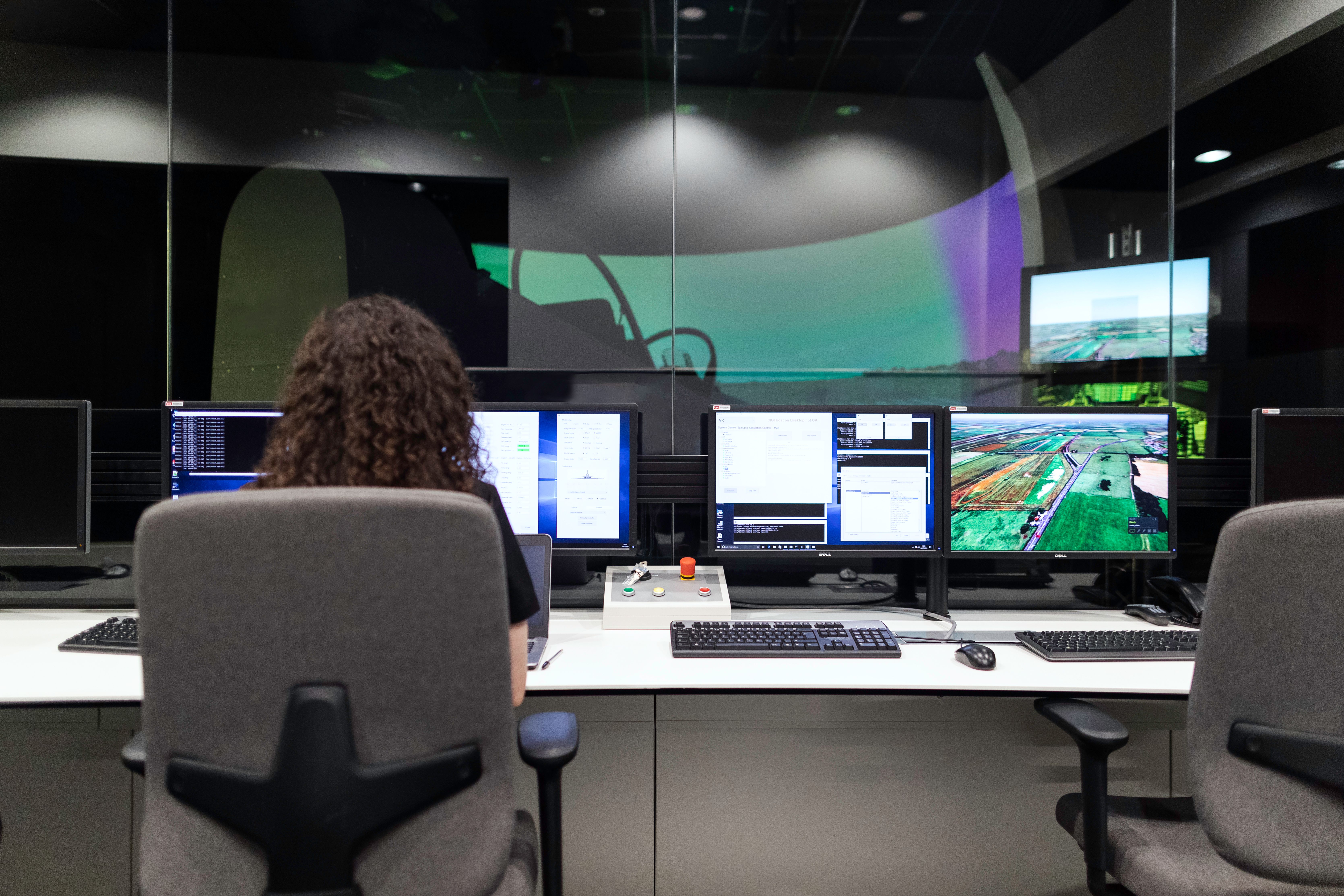 Analyst monitoring simulation and operational systems across multiple workplace screens